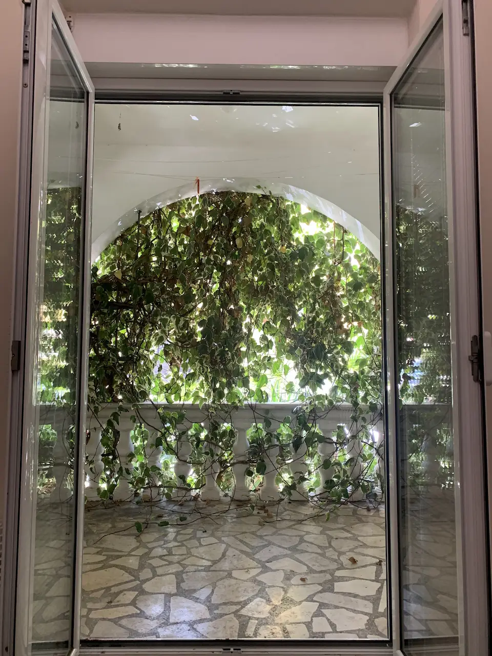 Open glass doors to a vine-covered balcony and stone floor
