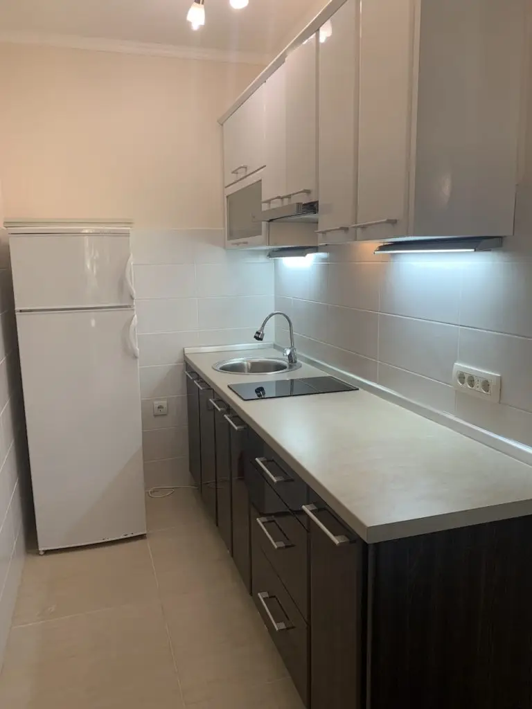 Compact kitchen with white cabinets, refrigerator, sink, and stovetop