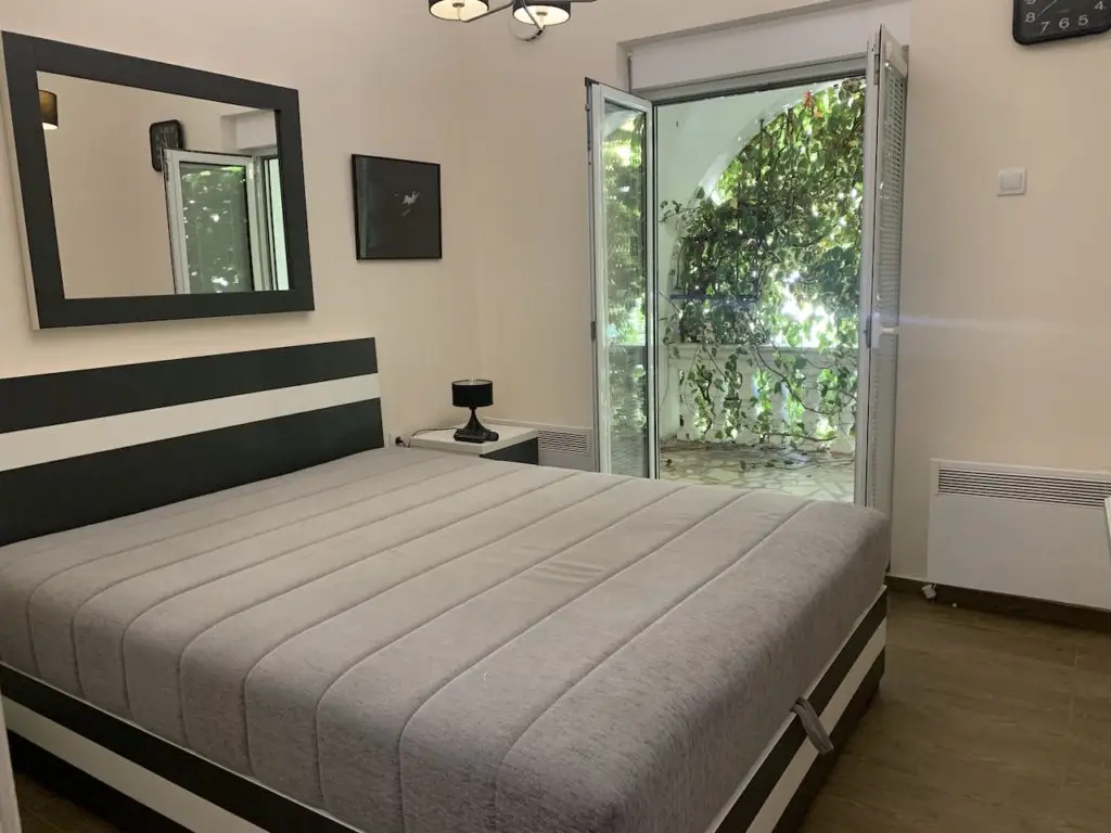Bedroom with bed, mirror, and open door to leafy balcony