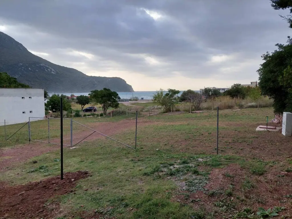 Vacant grassy lot with fence posts by the sea and mountain
