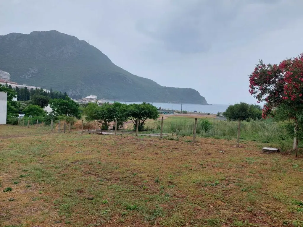 Grassy plot with fence, trees, mountain, and sea view