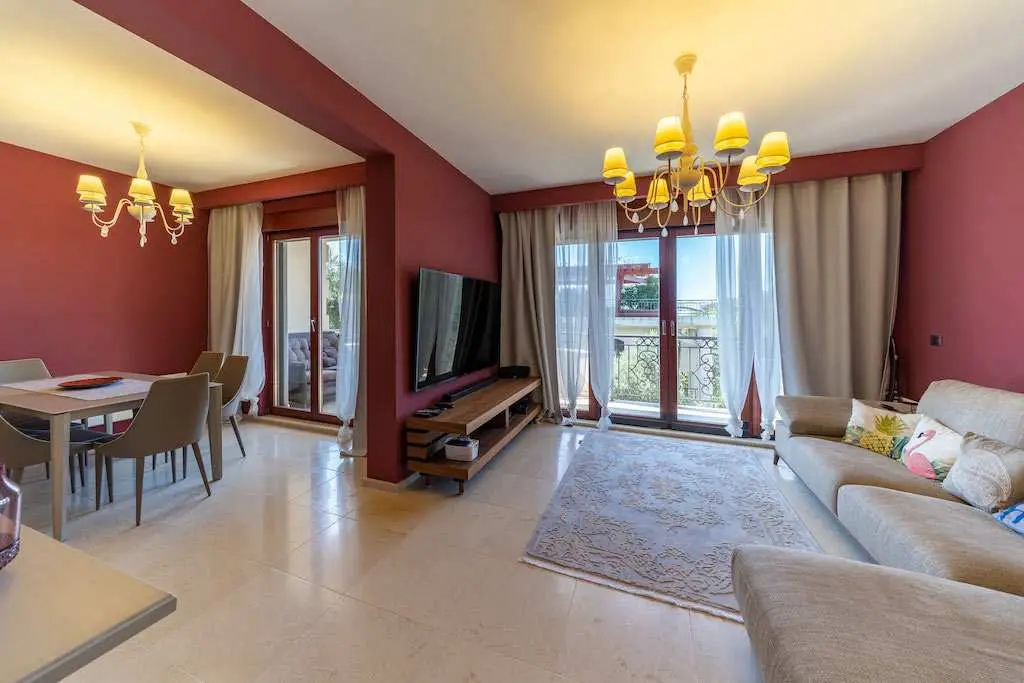 Living room with beige sofa, dining table, TV, and balcony doors
