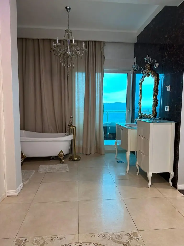 Elegant bathroom with freestanding tub, chandelier, and sea-view balcony