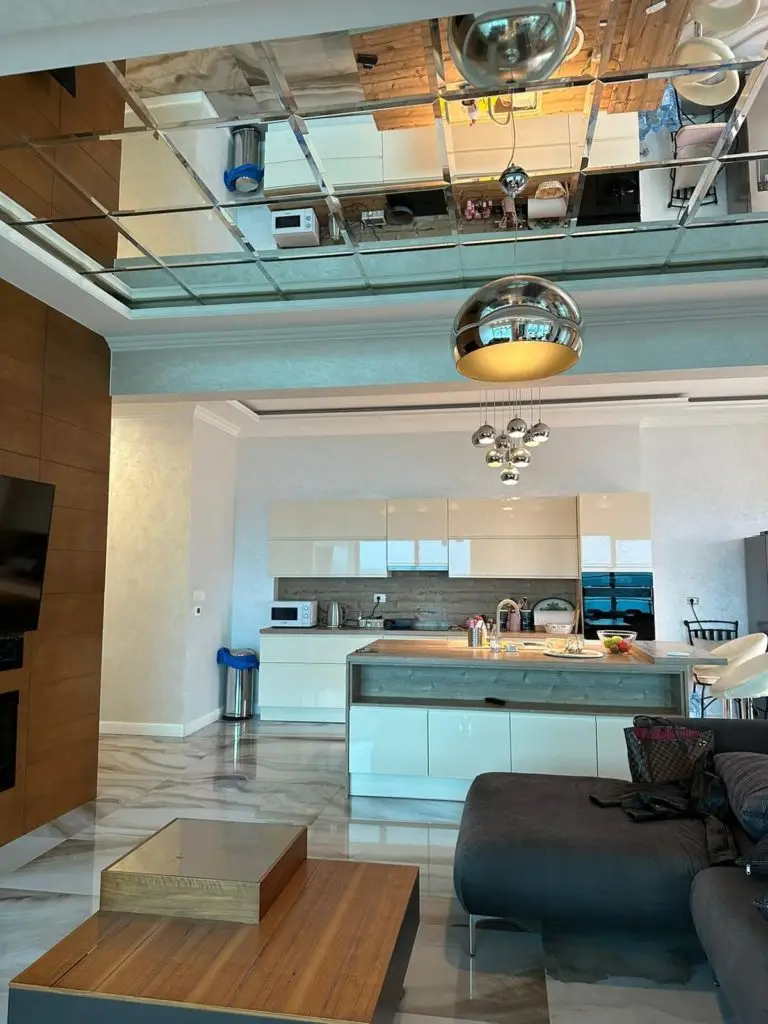 Modern open-plan kitchen and living room with mirrored ceiling, island, and sofa