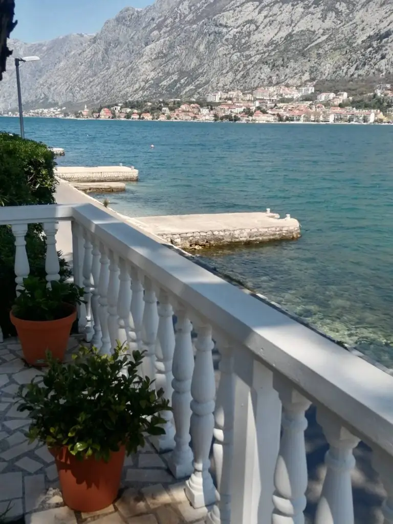 Seaside terrace with white railing, potted plants, and mountain bay view