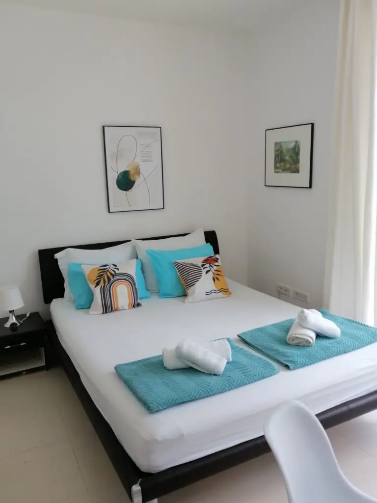 White bedroom with bed, turquoise towels, and framed wall art