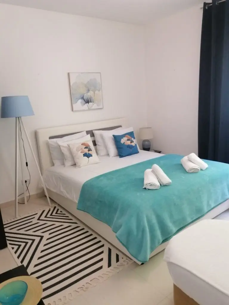 Modern bedroom with white bed, turquoise throw, and blue floor lamp