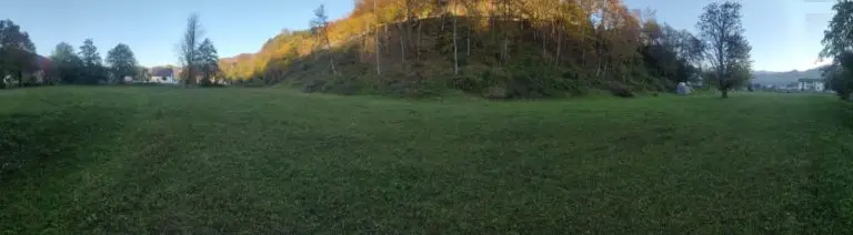 Wide grassy field with wooded hill and scattered trees