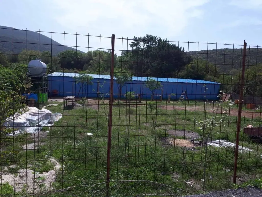 Fenced grassy lot with blue building and hills