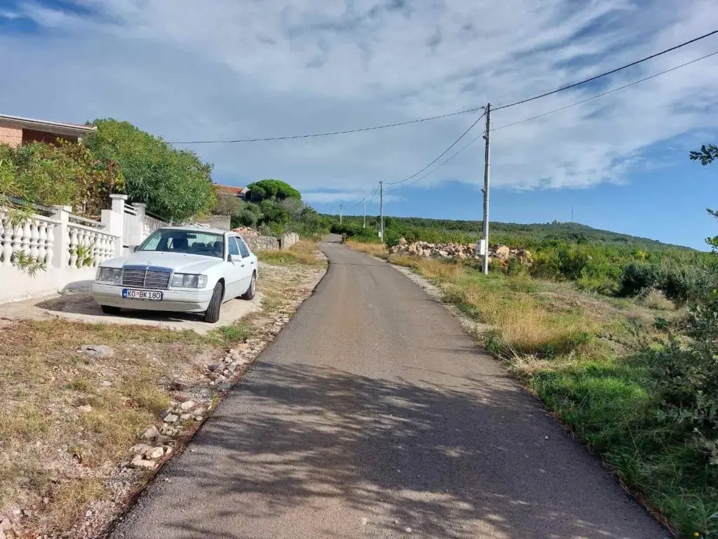 Rural paved road curving past white sedan and house fence