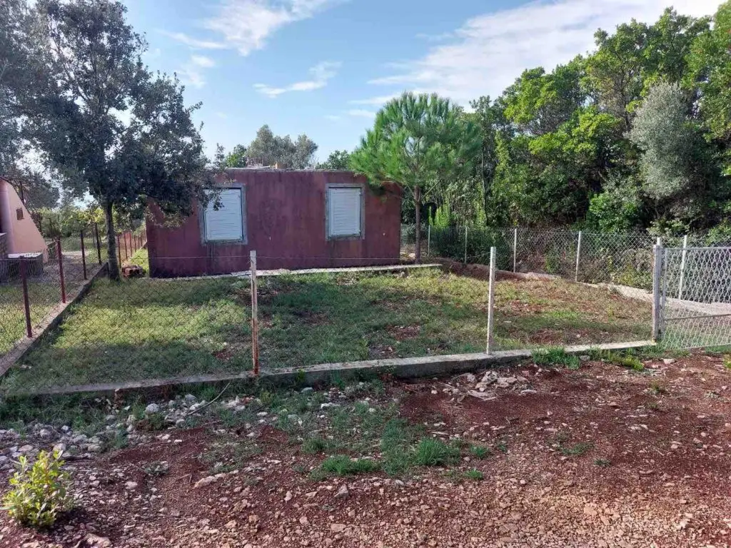 Small purple house with shuttered windows and fenced grassy yard