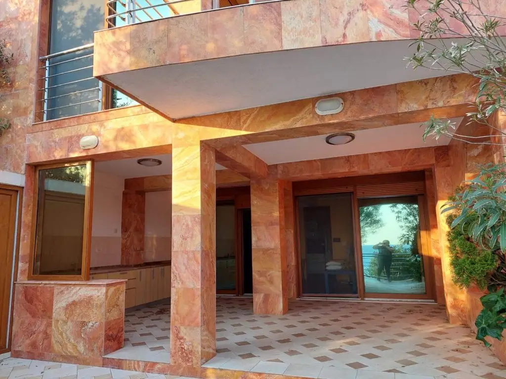 Stone-clad villa patio with sliding glass doors and sea reflection