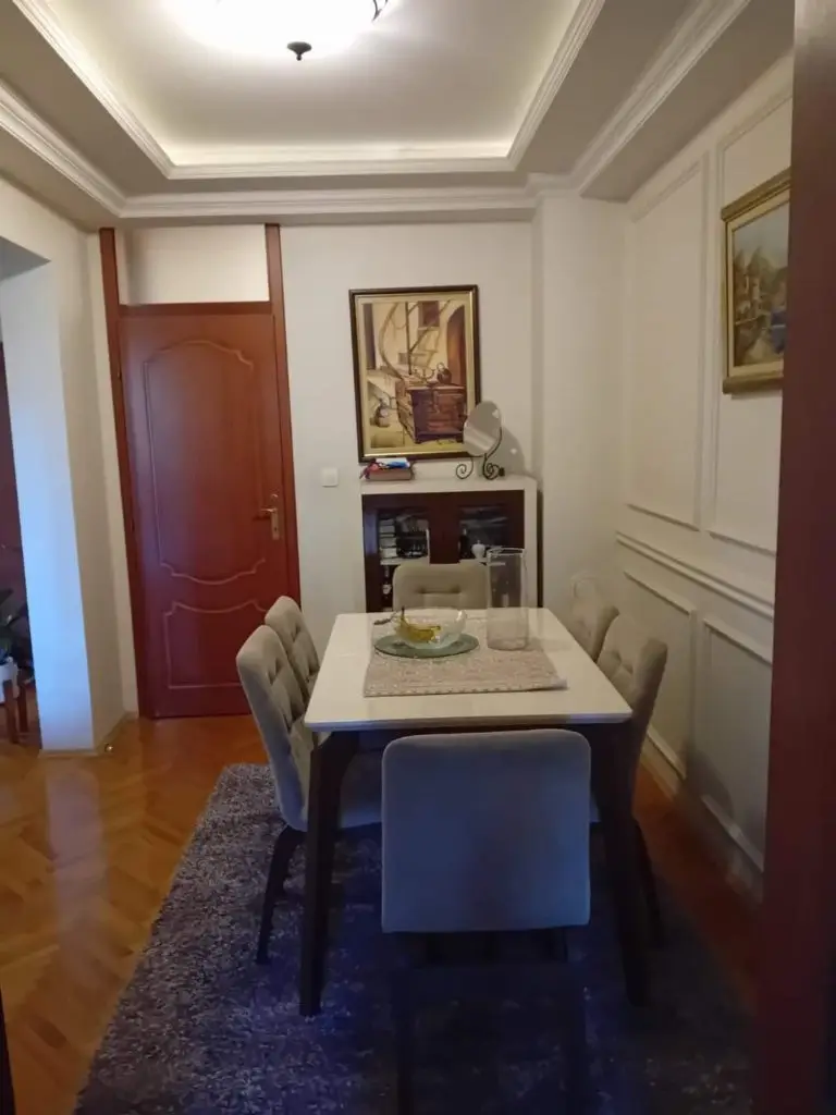 Dining area with white table, beige chairs, and red door