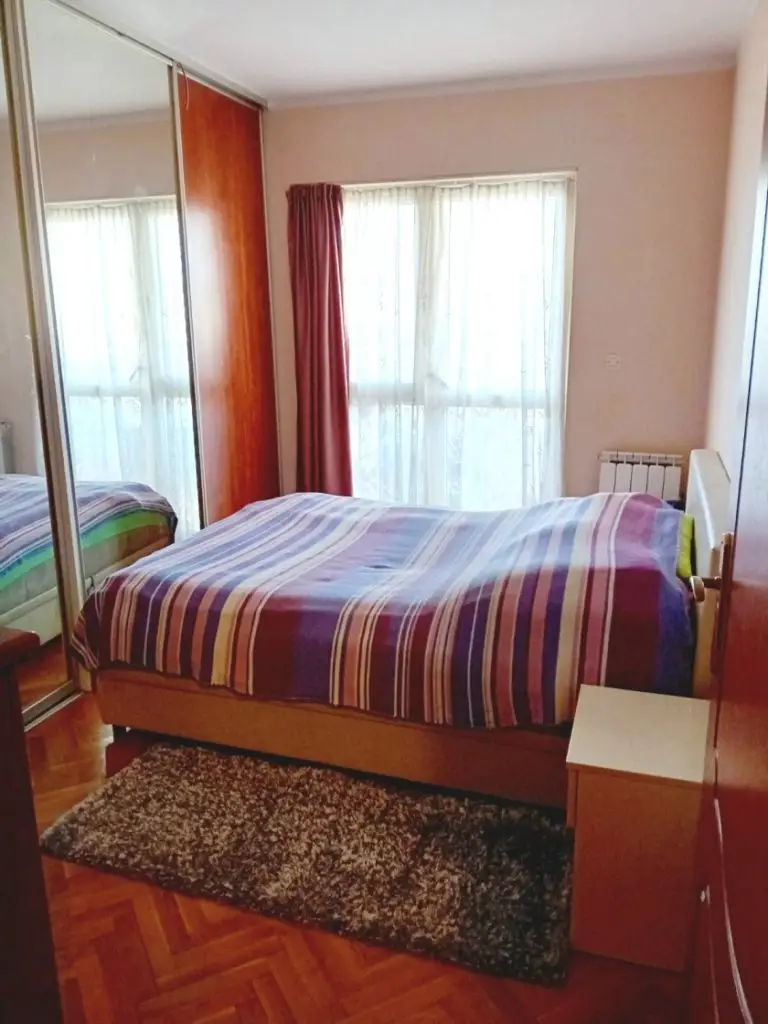 Bedroom with striped bedspread, mirrored wardrobe, and window curtains