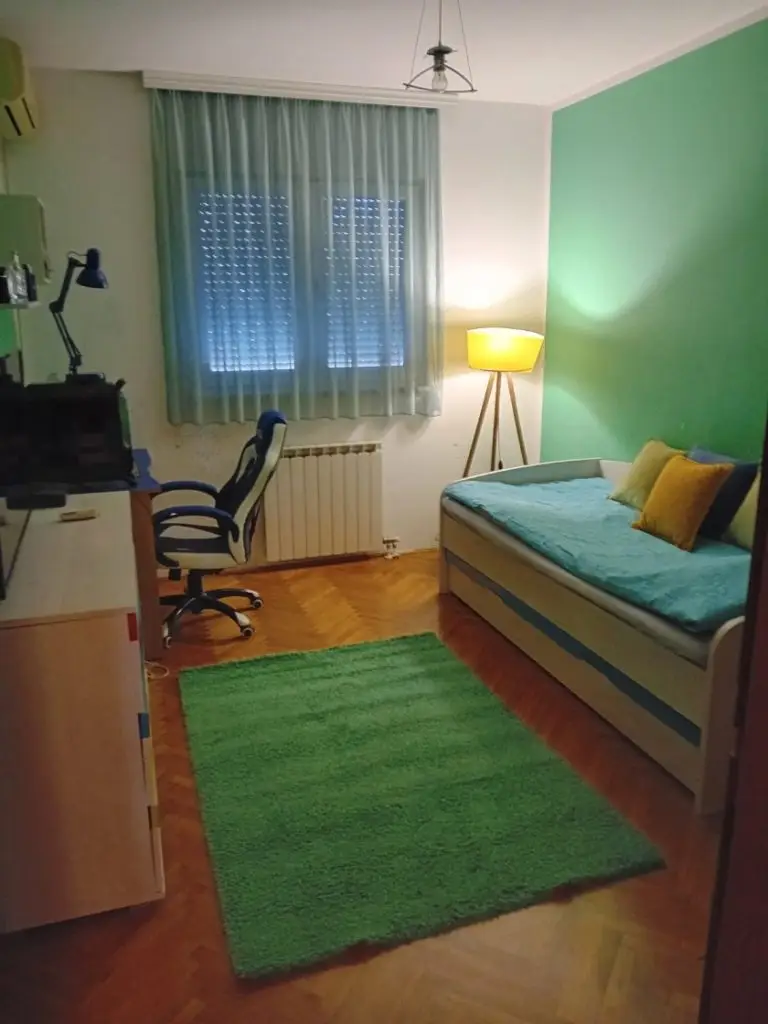 Small bedroom with bed, desk, chair, lamp, and green rug