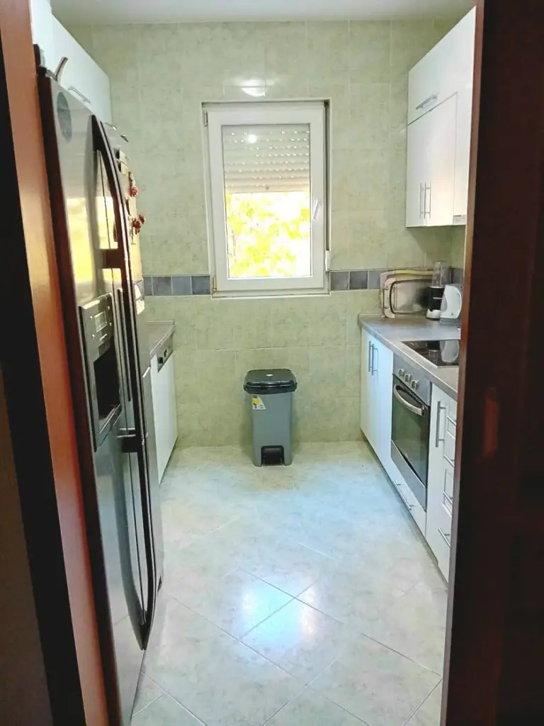 Narrow modern kitchen with refrigerator, oven, and window