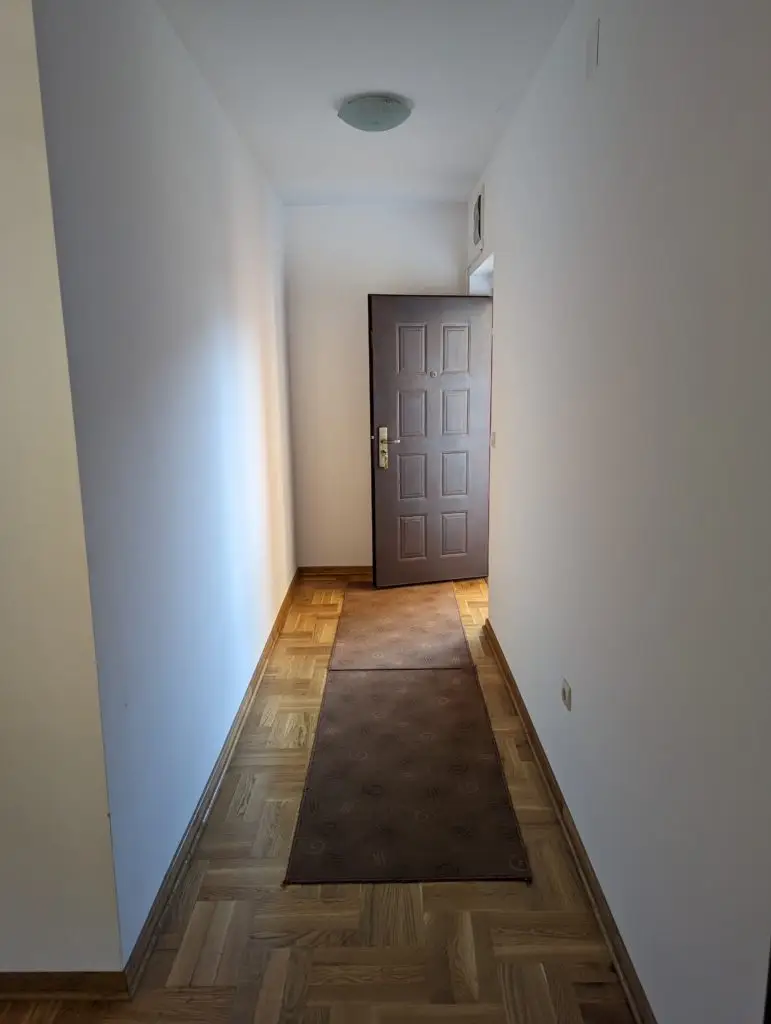 Narrow hallway with open brown front door and runner rug