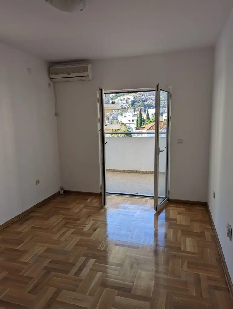 Empty room with parquet floor, open balcony door, air conditioner