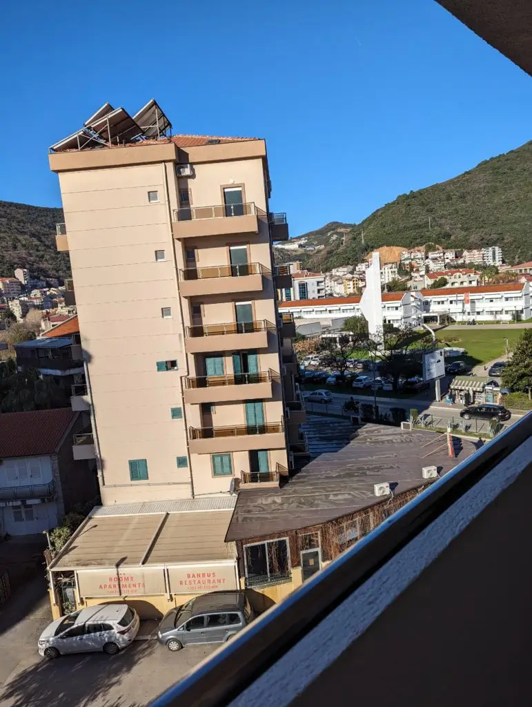 Tall beige apartment building with balconies beside mountains and clear sky
