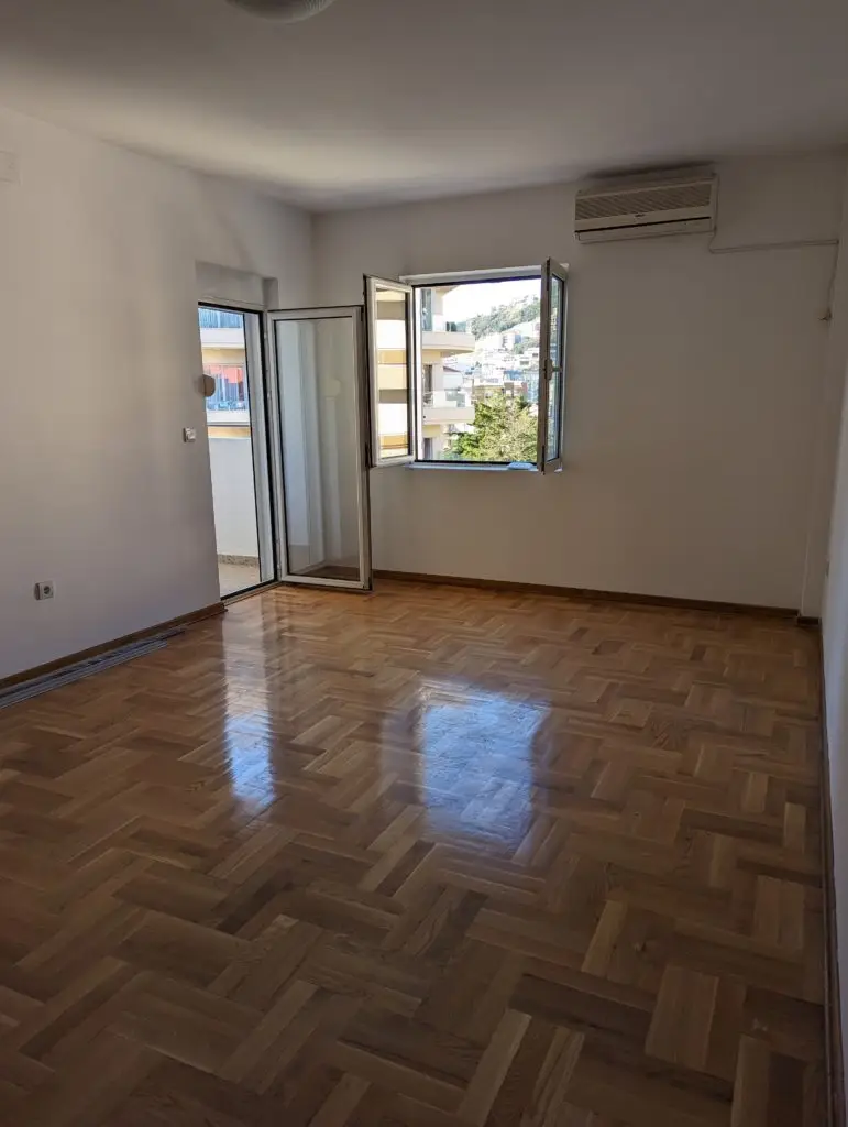 Empty room with parquet floor, open balcony door, and wall air conditioner