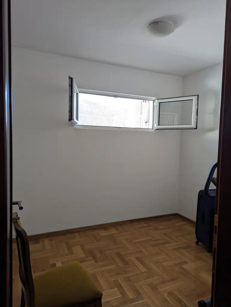 Small empty room with open window and herringbone wood floor