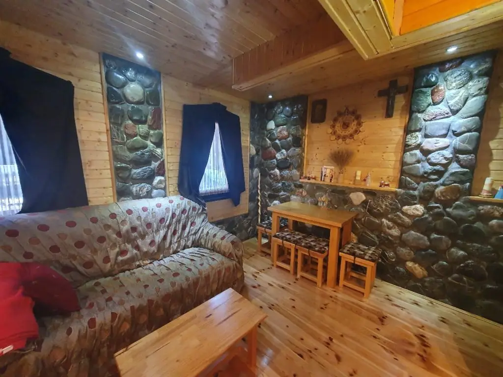 Rustic wood-paneled living room with stone walls, sofa, table, and stools