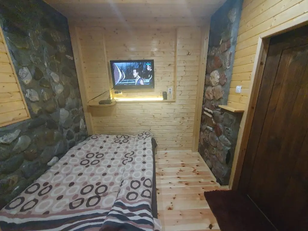 Cozy wooden bedroom with stone walls, bed, and wall-mounted TV