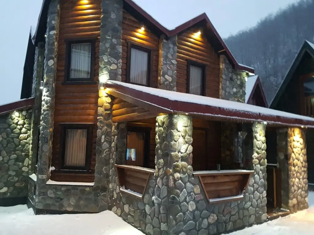 Snow-covered stone and log chalet with lit exterior lights