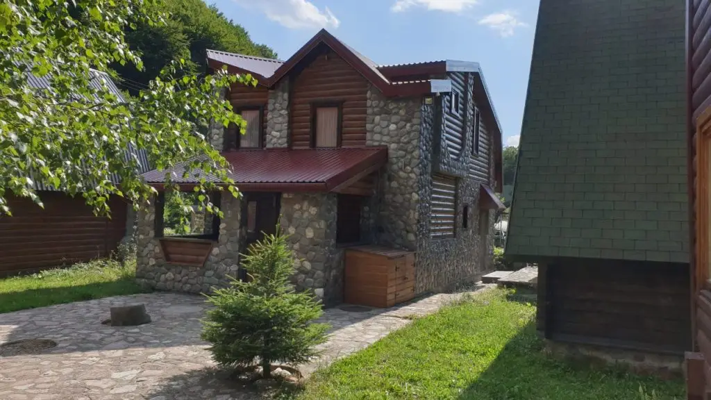 Stone-and-log house with red roof and courtyard tree