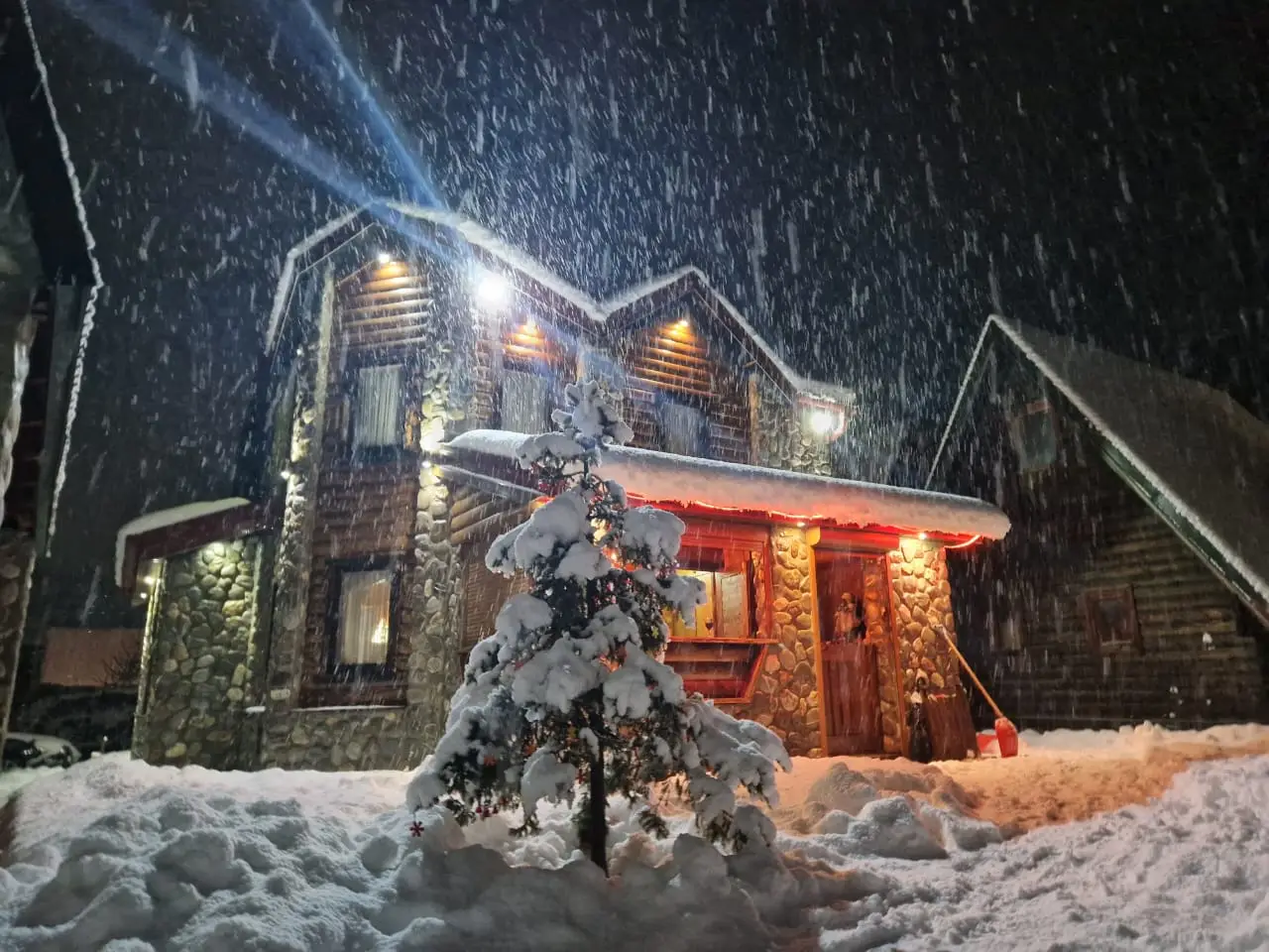 Snow-covered house at night with falling snow and lit porch