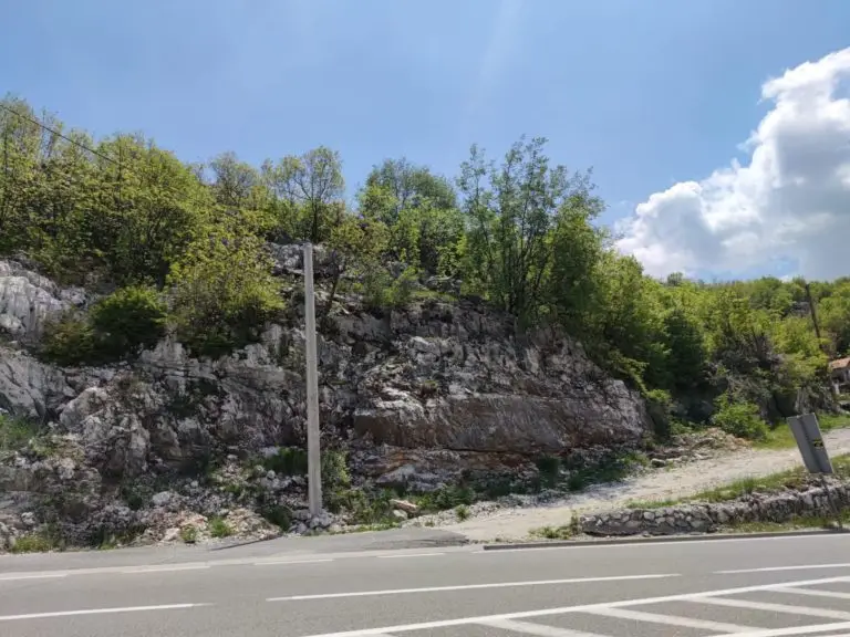 Rocky hillside beside a road with trees and blue sky