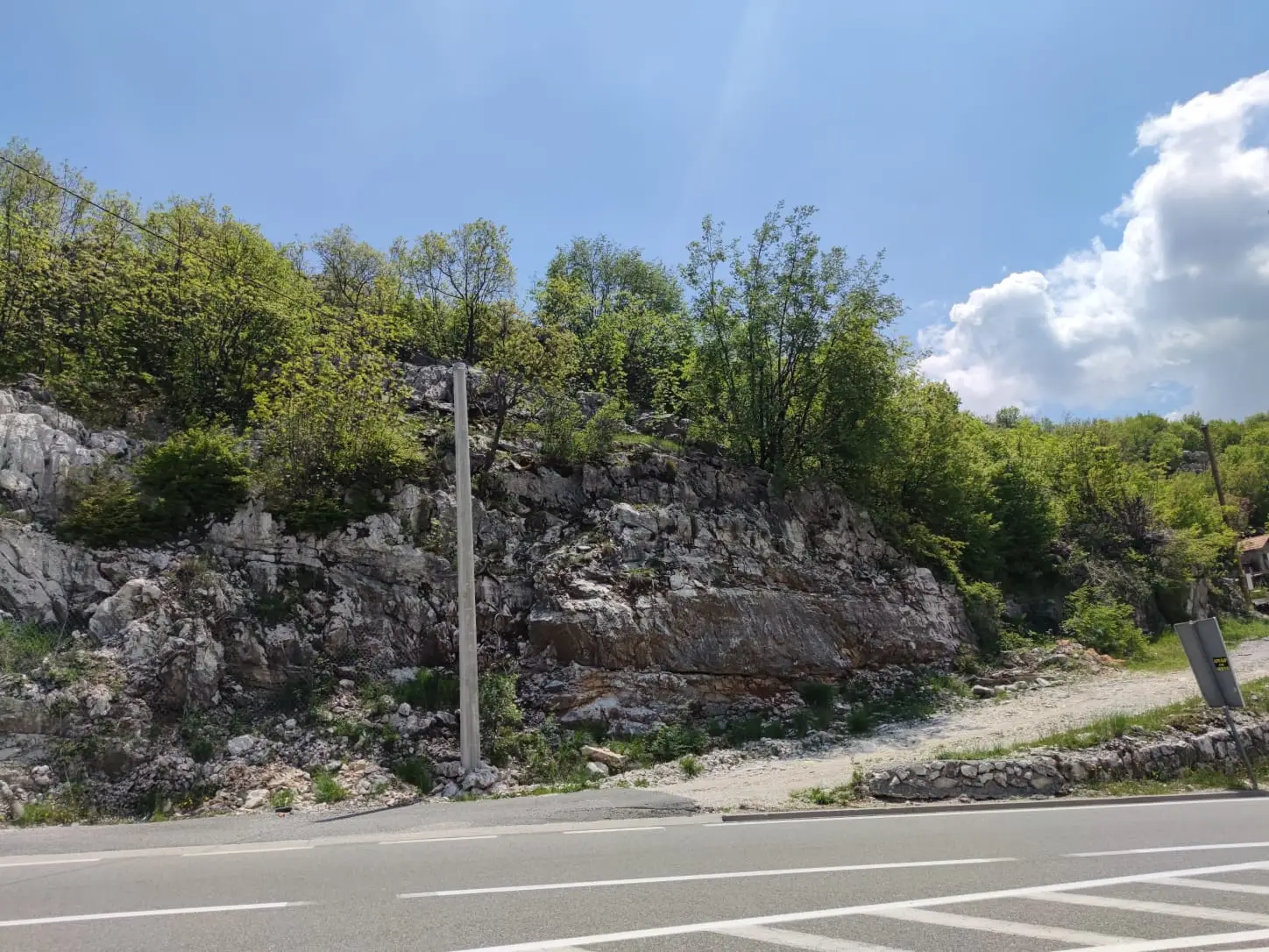 Rocky hillside beside a road with trees and blue sky