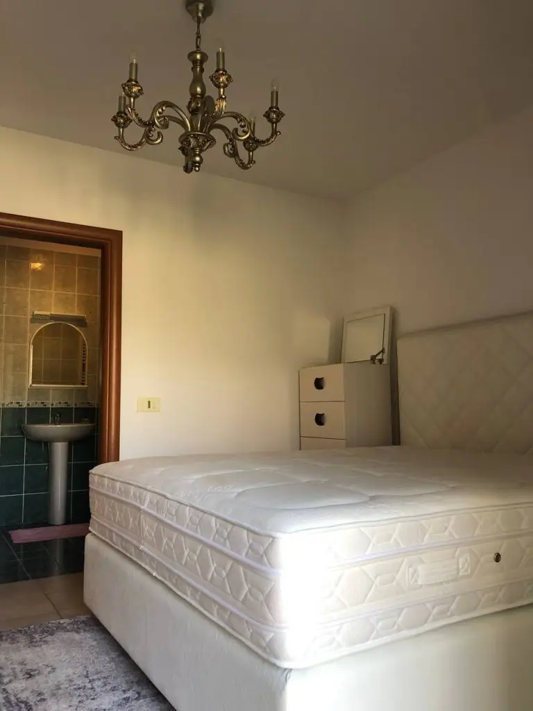 Bedroom with white bed, chandelier, and bathroom doorway
