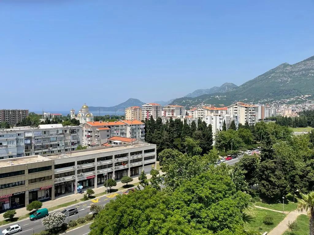 City buildings, trees, mountains, and sea under clear sky