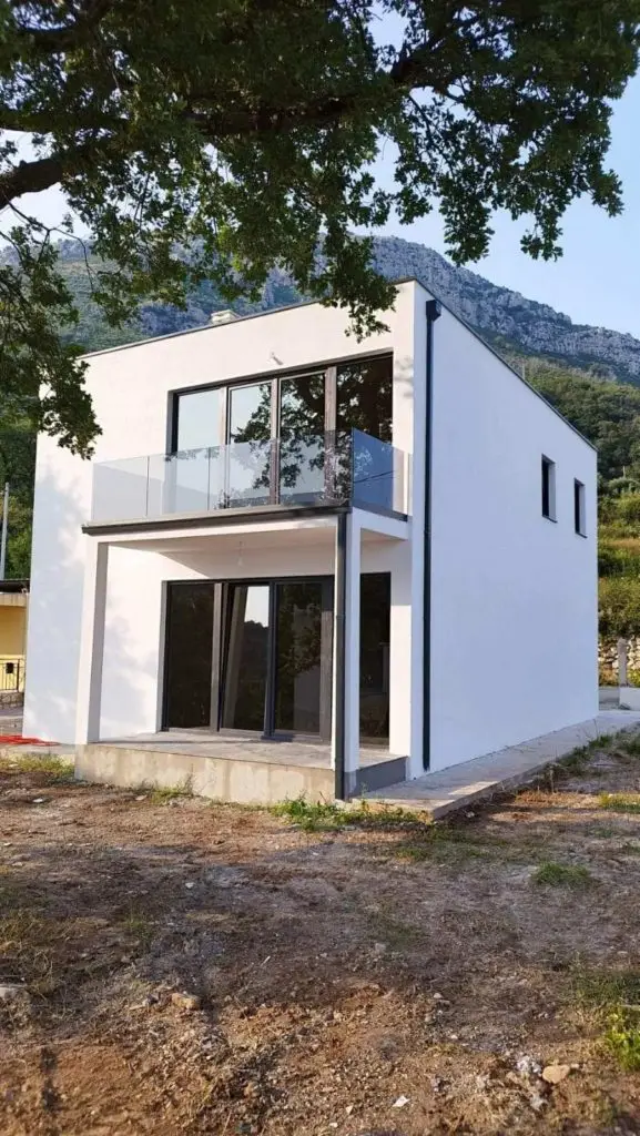 Modern white two-story house with balcony and mountains behind