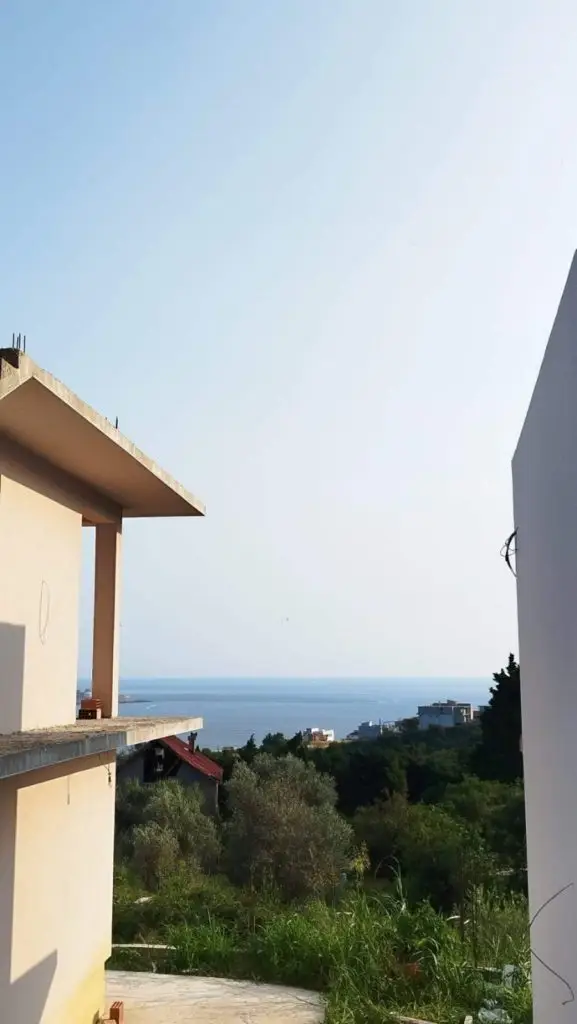 View between unfinished buildings toward the sea and greenery