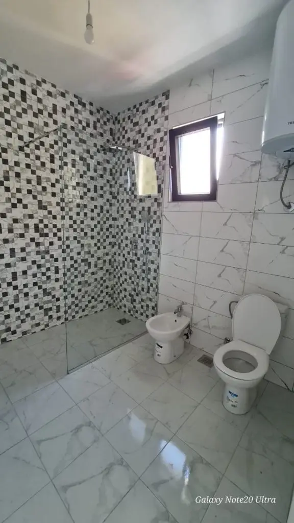 Tiled bathroom with glass shower, toilet, bidet, and small window