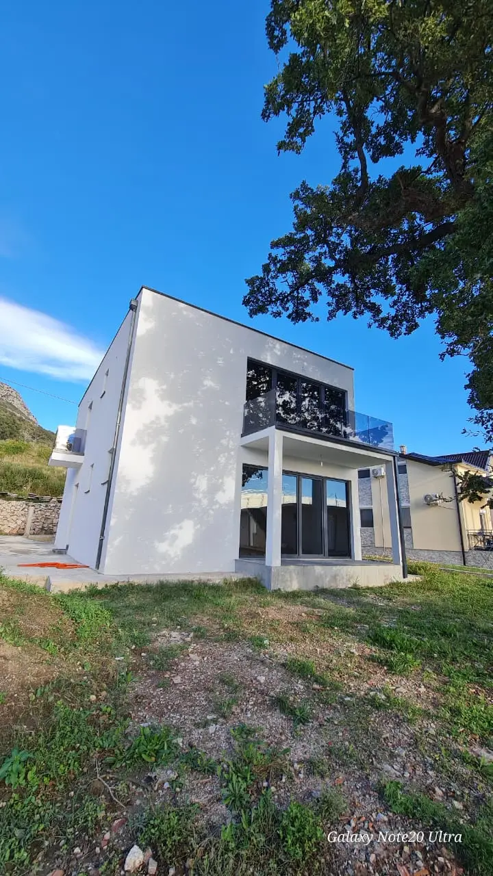 Modern white two-story house with black windows and balcony, grassy yard