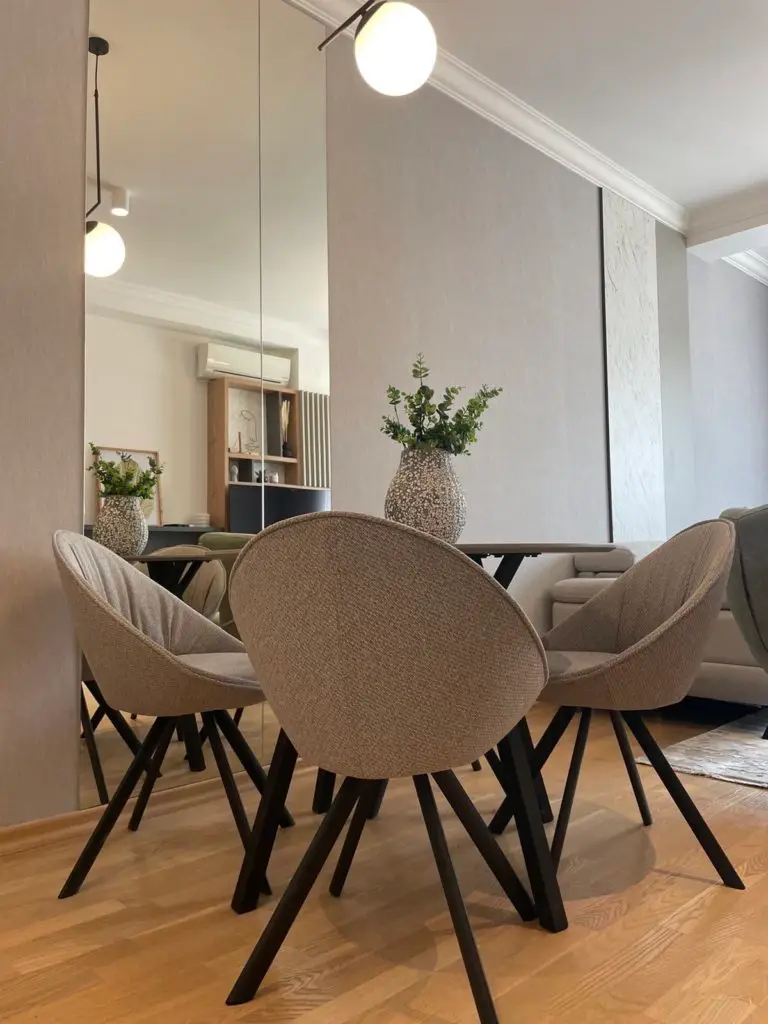Beige dining chairs around a table with vase and mirror reflection