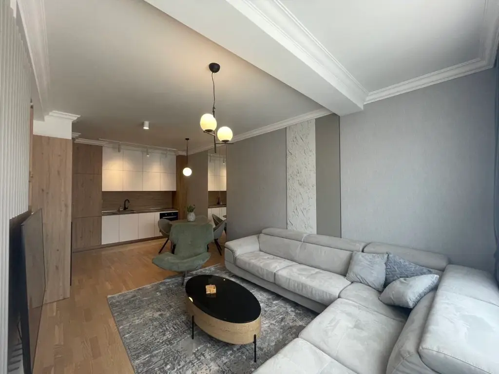 Modern open-plan living room with gray sectional and kitchen.