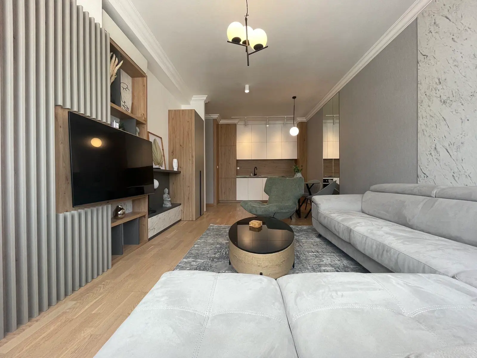 Modern living room with gray sofa, TV, and kitchen view
