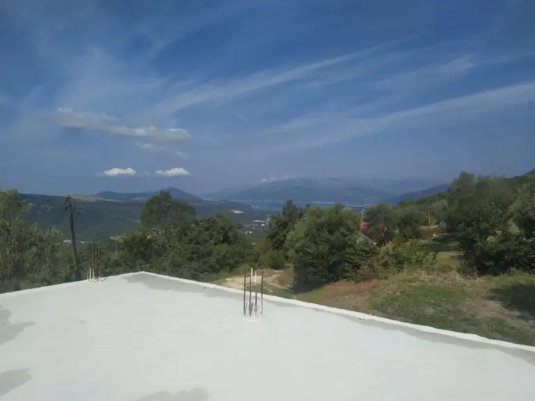 Flat white roof overlooking trees, mountains, and blue sky