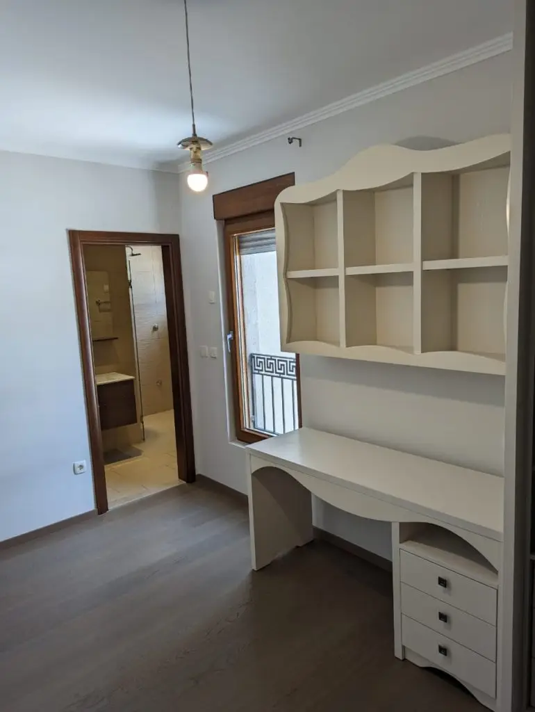 Small room with white desk, shelves, and bathroom doorway