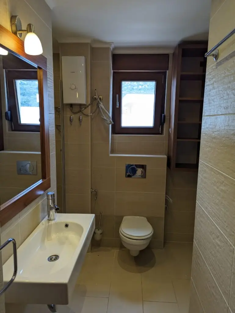 Small beige bathroom with sink, toilet, and windows