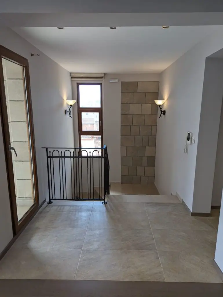 Tiled hallway landing with staircase railing and wall sconces