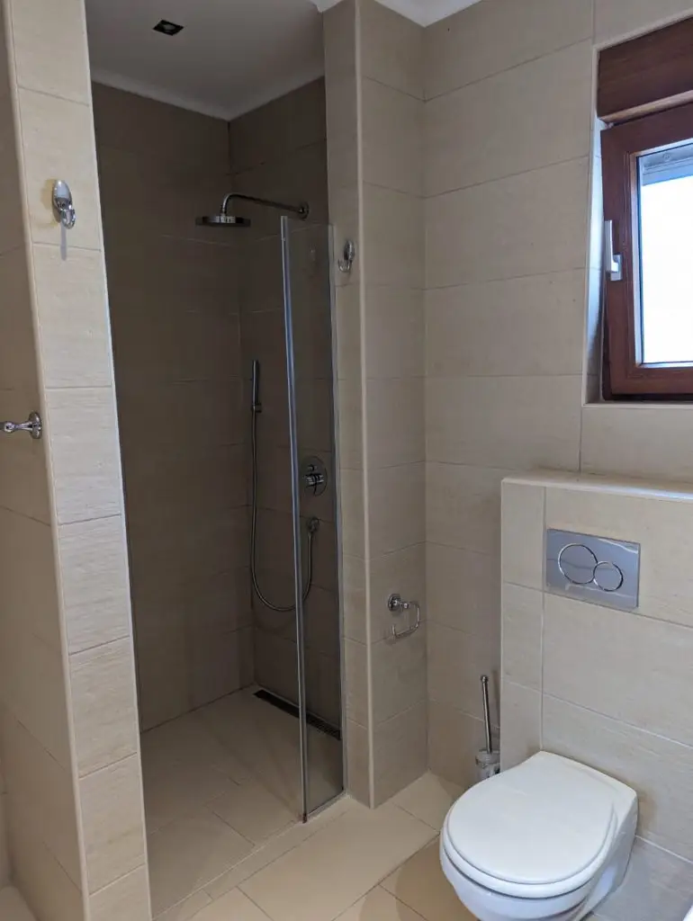Beige tiled bathroom with shower and white toilet