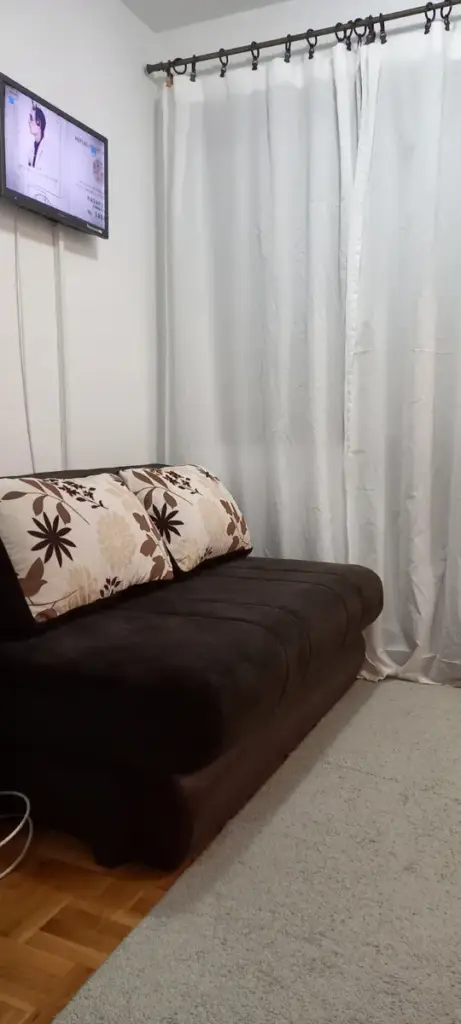 Brown sofa with patterned cushions, wall-mounted TV, and white curtains