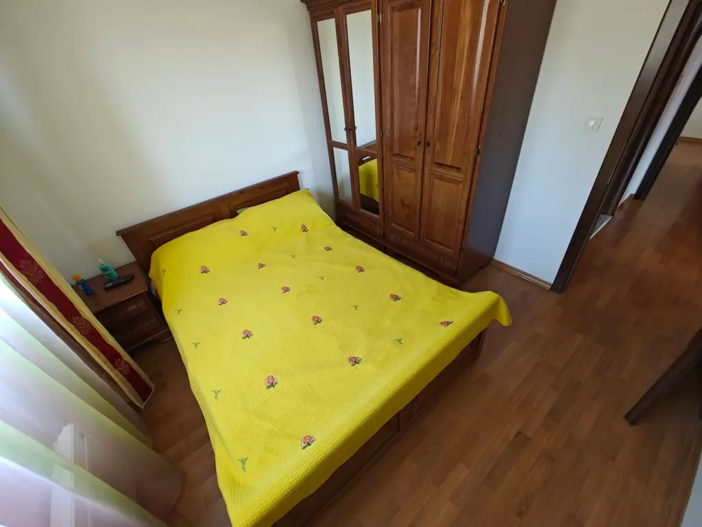 Bedroom with yellow bedspread, wooden wardrobe, and nightstand