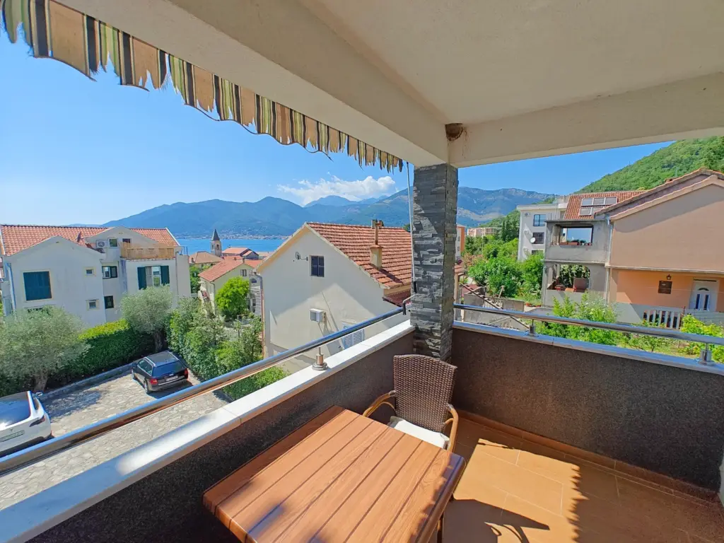 Balcony with table and chair overlooking houses, sea, and mountains