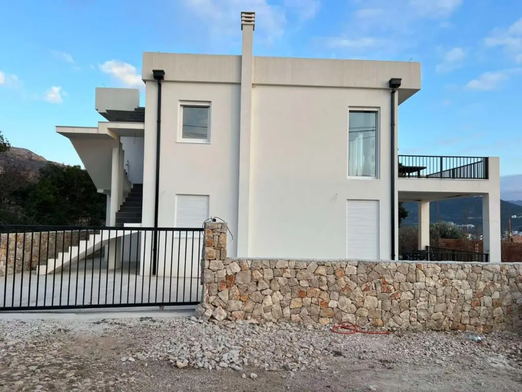 Modern white two-story house with stone wall and black gate
